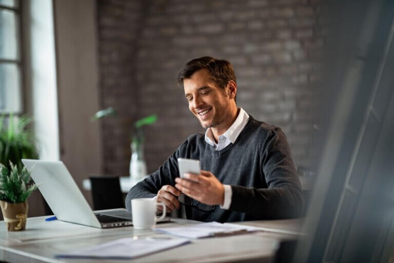 Homem sorrindo enquanto usa o celular em um escritório