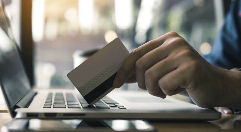 Uma mão segurando um cartão de crédito que encosta em um teclado de notebook.